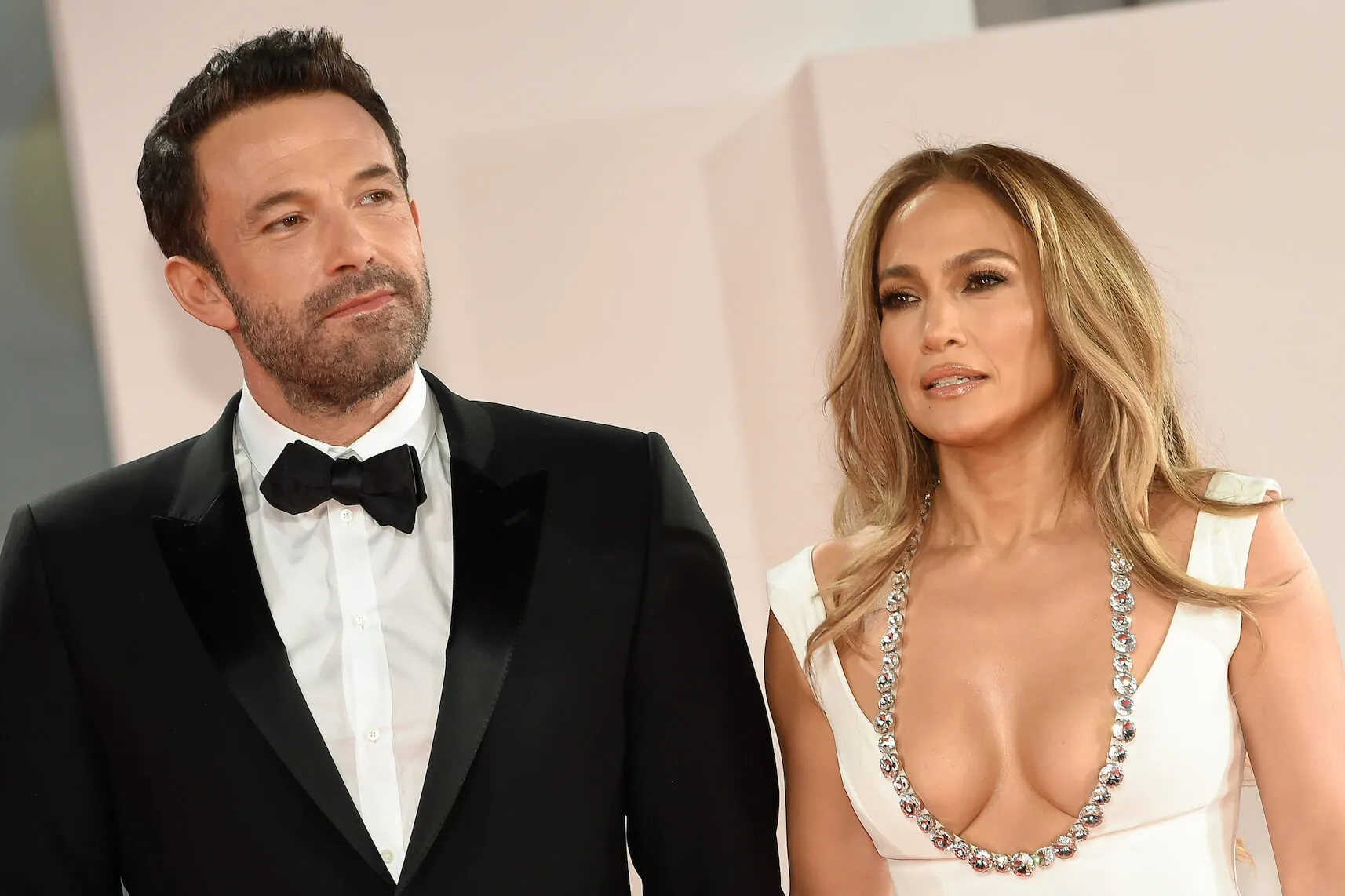 Ben Affleck in a black suit with a white undershirt and black bow tie next to Jennifer Lopez in a white low-cut dress