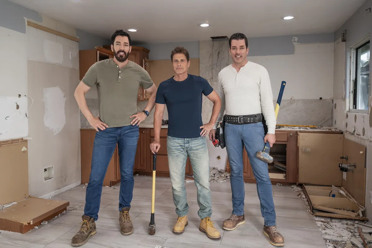 Drew Scott, Rob Lowe, and Jonathan Scott standing in a kitchen and holding sledgehammers in a publicity shot for HGTV's 'Celebrity IOU'