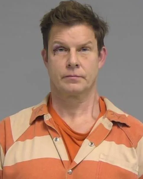 Eric Mabius mugshot, with black eye and wearing white and orange prison jumpsuit