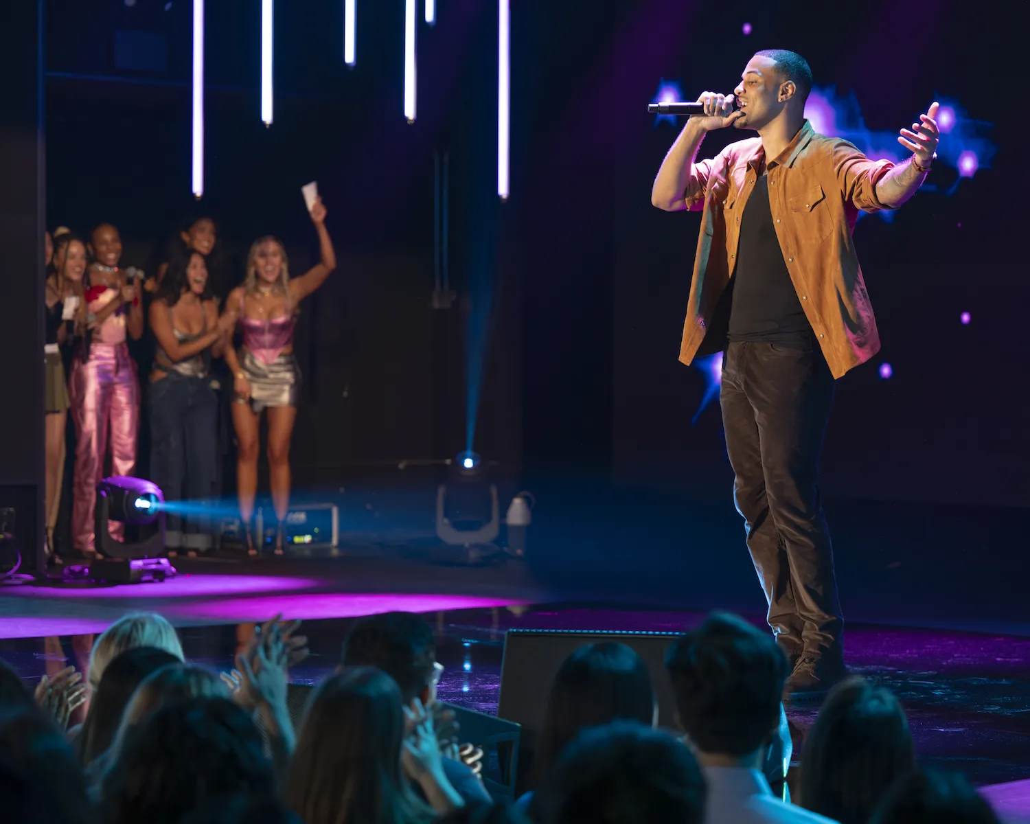 'The Bachelor' Season 29 star Grant Ellis singing into a microphone while standing on stage. The women on his date are in the background cheering for him.