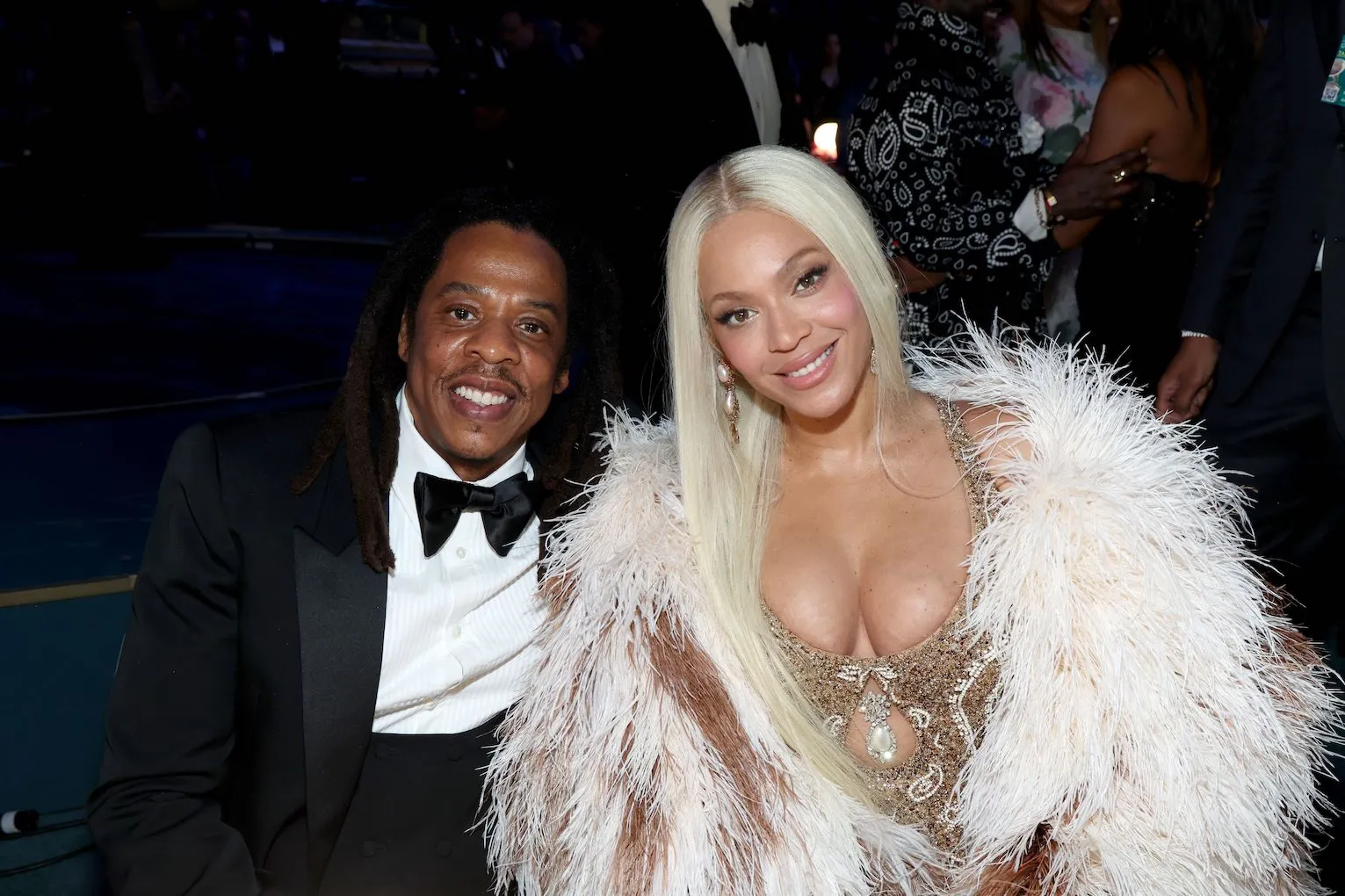 Jay-Z in a tuxedo smiling beside Beyoncé, who's in a fur coat and gold dress, at the Grammy Awards