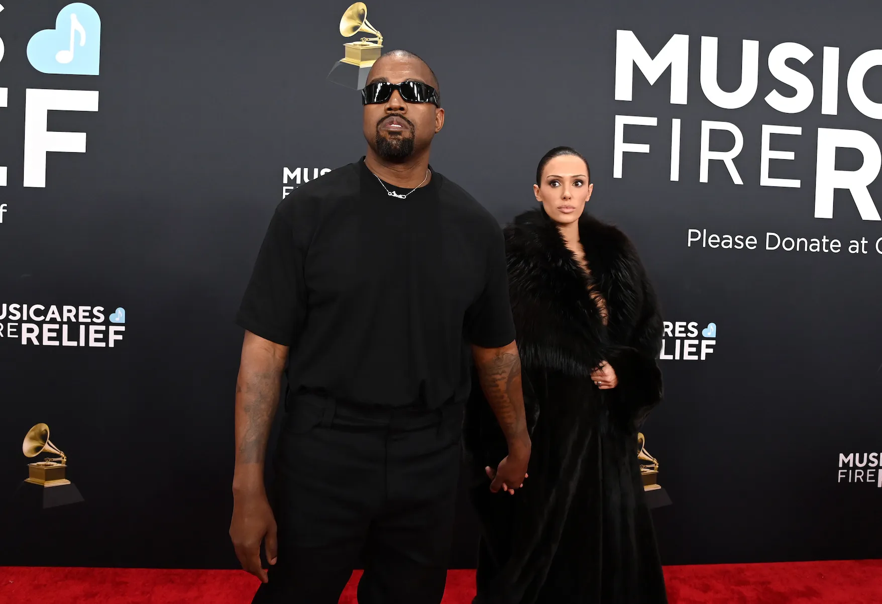 Kanye West in all black standing in front of Bianca Censori in a fur coat on the red carpet