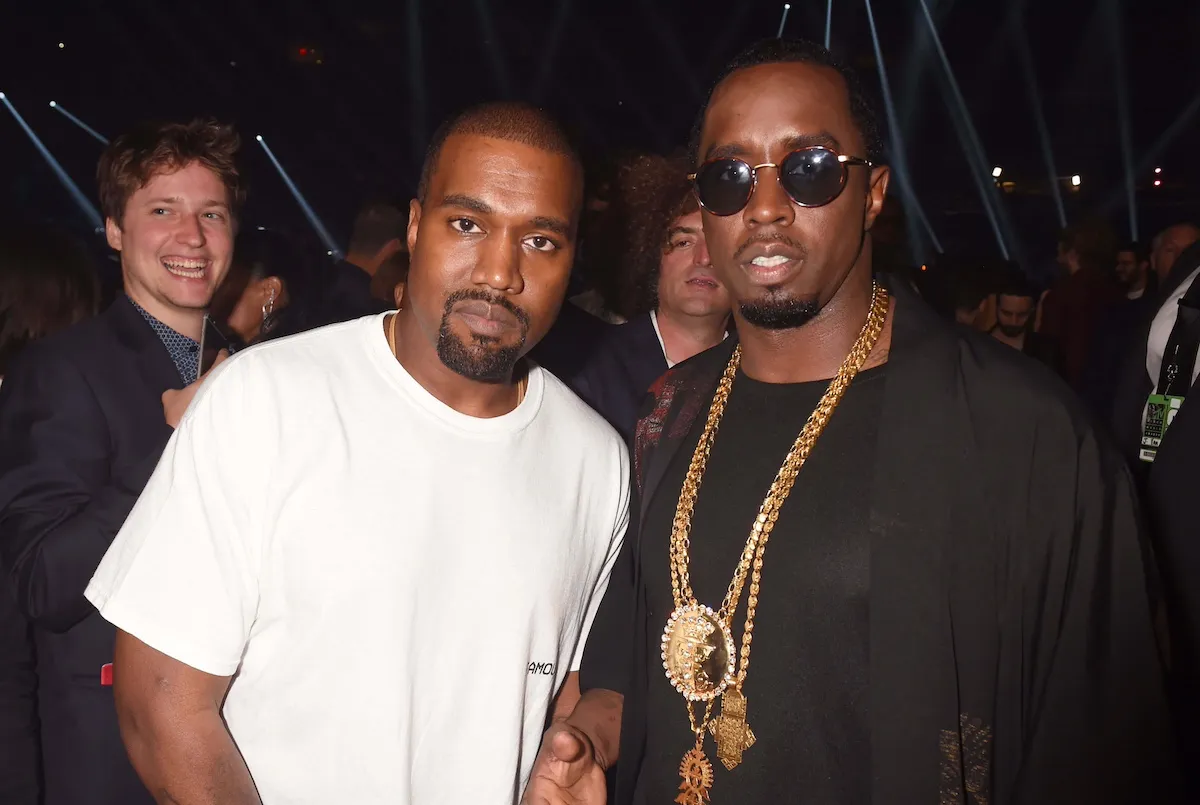 Kanye West in a white T-shirt and Sean 'Diddy' Combs in a black shirt with sunglasses and gold chains posing side by side against a dark background