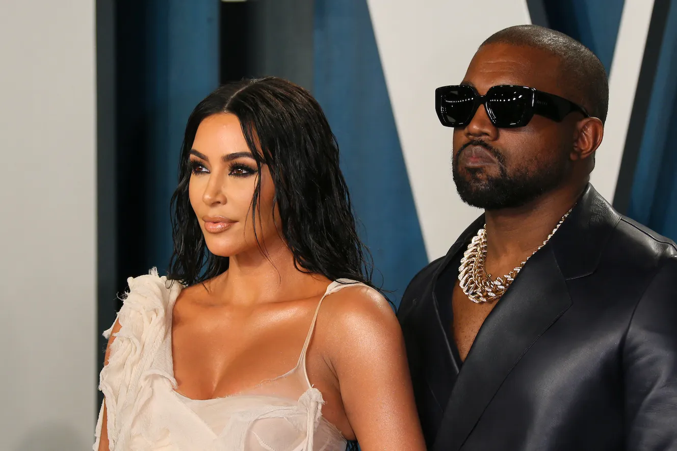 Kim Kardashian in a white dress next to Kanye West in a black suit and sunglasses at a Vanity Fair Oscar party in 2020