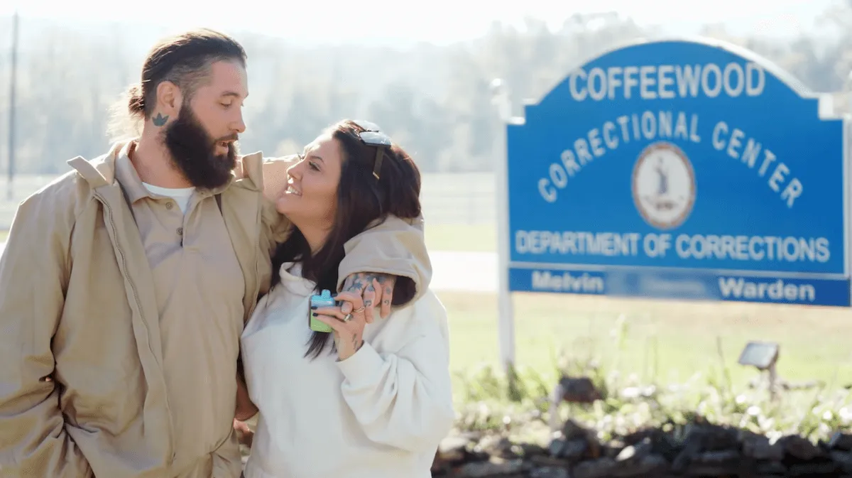 Man with his arm around a woman standing in front of a prison sign in 'Love After Lockup'