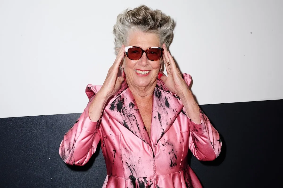 Wearing a pink satin dress, Prue Leith smiles backstage before the VIN + OMI London Fashion Week show