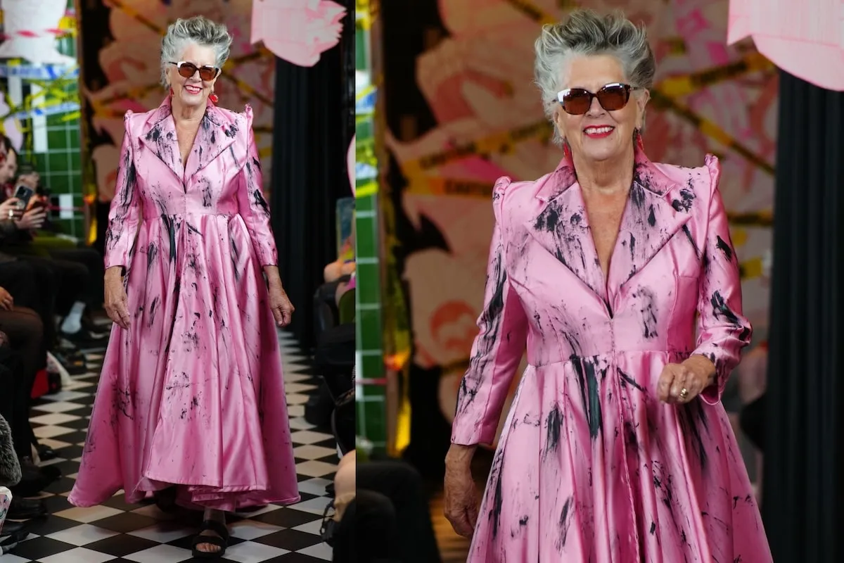 Wearing a pink satin dress, Prue Leith smiles and walks on the catwalk during the VIN + OMI London Fashion Week show