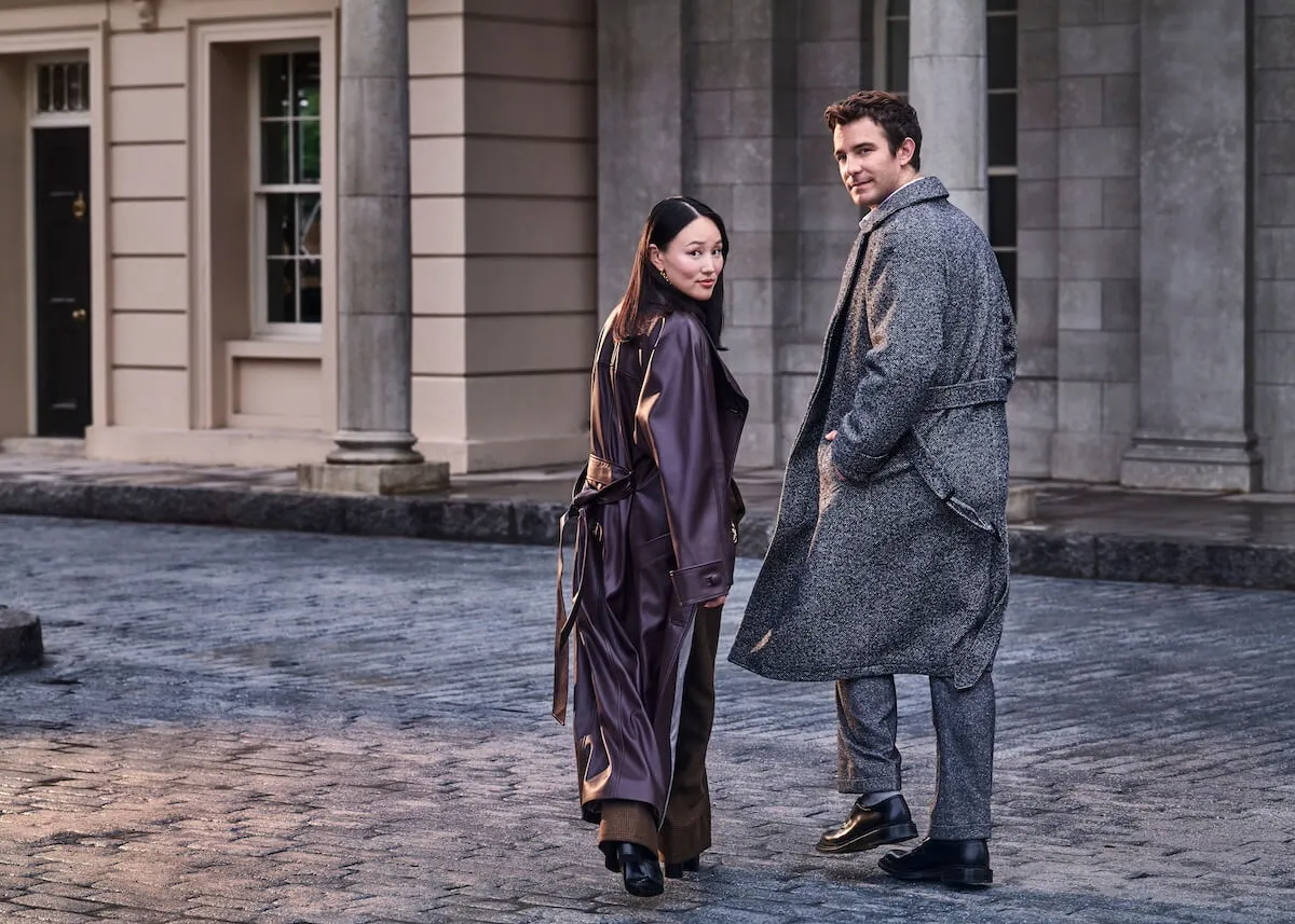 Yerin Ha and Luke Thompson of 'Bridgerton' Season 4 walking on a cobblestone street and looking over their shoulders