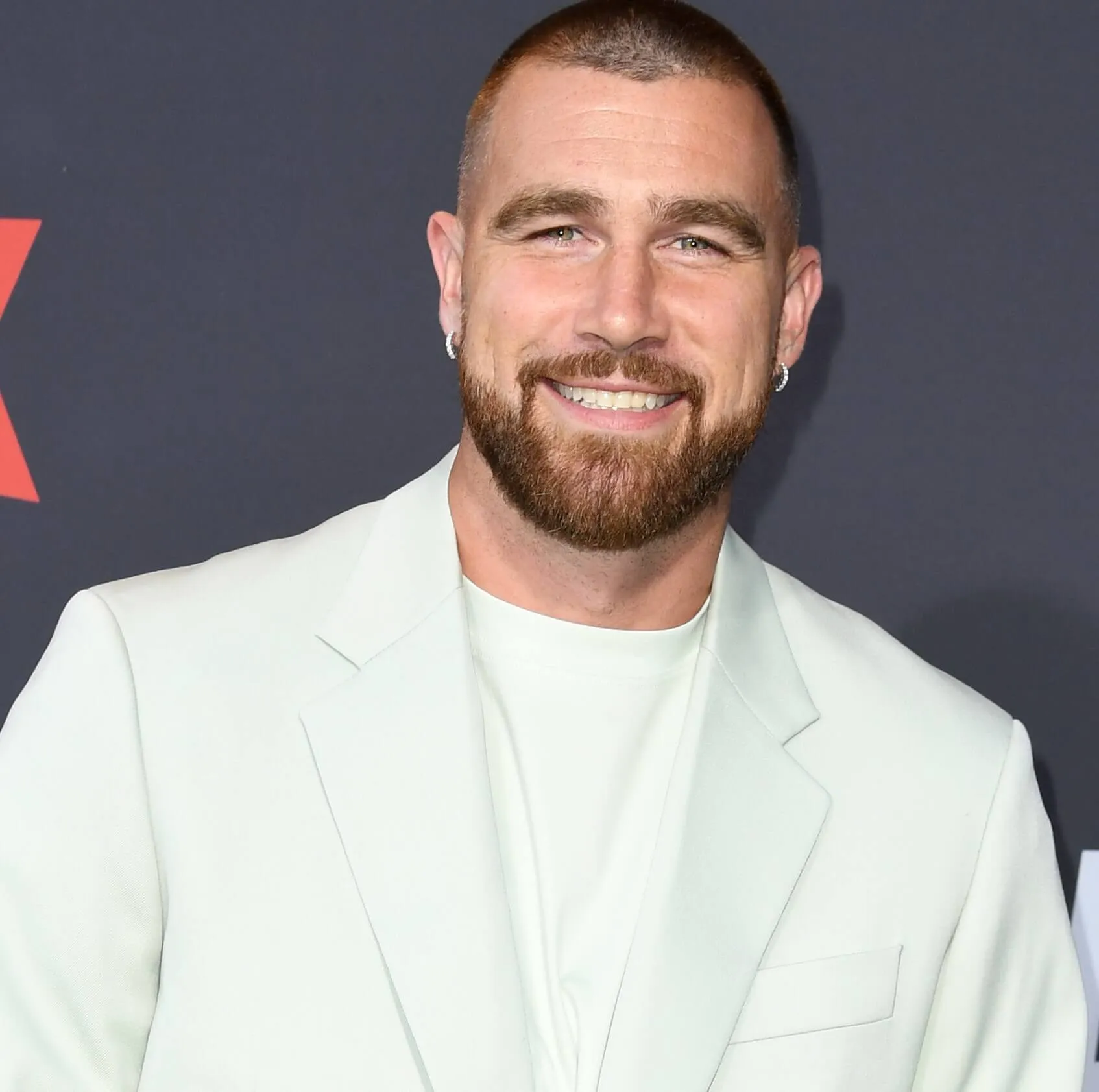 Travis Kelce wears a white shirt and white suit jacket.